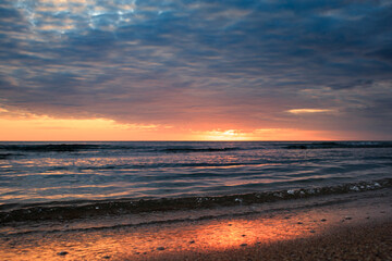 Naklejka na ściany i meble Coast of the Caspian Sea at sunset, pink-orange clouds, water, beach.