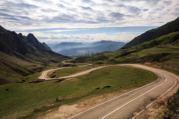 Naklejka premium A long winding mountain road, against the backdrop of high relief, sharp mountains. Mountain serpentine.