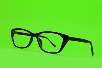 Spectacles with diopters in a black frame on a green background. Shallow depth of field