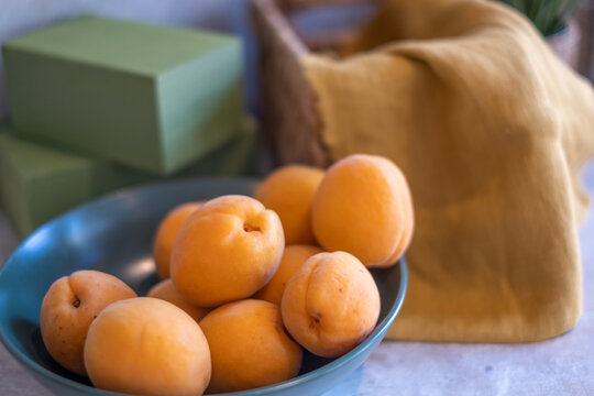 kitchen background with beautiful juicy yellow apricots in blue bowl on wooden table, green wooden box and khaki towel
