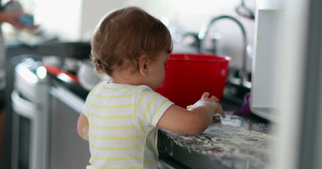 Baby playing covered with flour at kitchen, infant doing a mess with dough cooking