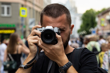 Portrait of young adult caucasian photographer taking a picture with a retro style camera against blurred crowded city street at background