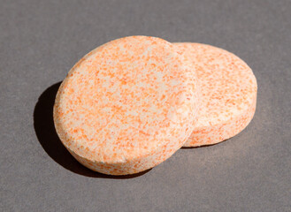 effervescent vitamins in round-shaped orange tablets on a naturally gray background with harsh shadows and light