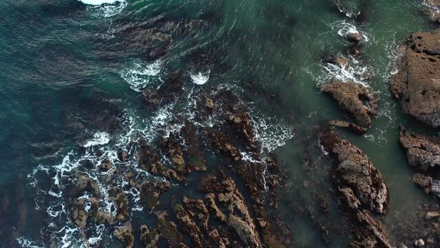 Aerial view of the ocean crashing into the rocks on the coast of swansea, mumbles UK. clear blue coast stunning views.