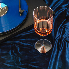 Wineglass with rose and vinyl lp on turntable composition on metalic blue background.Decadent party setting.