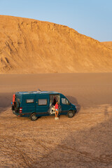 Woman standing next to her campervan in the desert at sunset