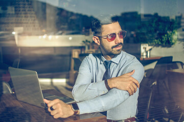 Portrait of handsome business man wearing sunglasses sitting in a cafe and looking through the...