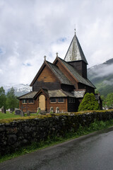 Fototapeta na wymiar Roldal, Norway - June 11, 2022: Medieval graveyard and Roldal wooden stave church. Roldal Stavkirke, 13th century. It is a parish church of the Church of Norway. Cloudy spring day. Selective focus