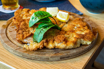 Breaded schnitzel on a wooden plate with lemon