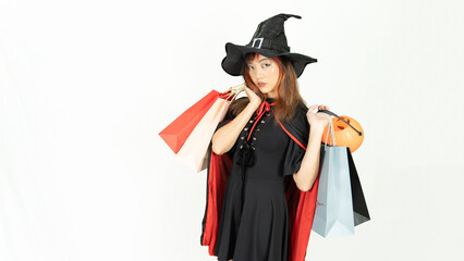 Young asian girl with black and orange hair  in black dress and witch hat is holding shopping bags and smiling on white background for Halloween day.