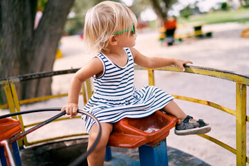 Little girl in sunglasses sits on a carousel with her back turned. High quality photo