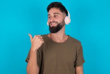young bearded hispanic man wearing casual clothes over blue background listens audio track via...