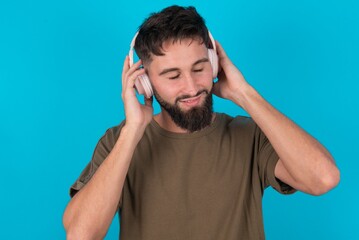 young bearded hispanic man wearing casual clothes over blue background wears stereo headphones listens music concentrated aside. People hobby lifestyle concept