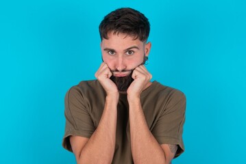 Portrait of sad young bearded hispanic man wearing casual clothes over blue background hands face