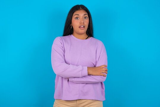 Shocked embarrassed Young beautiful hispanic woman wearing casual clothes over blue background keeps mouth widely opened. Hears unbelievable novelty stares in stupor