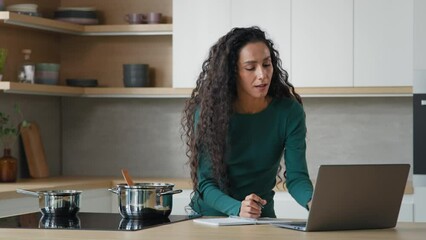 Arabian woman mother cooking lunch meal healthy food in modern kitchen writing internet recipe using helpful cookery website on laptop cookbook menu app watching online tutorial culinary video at home
