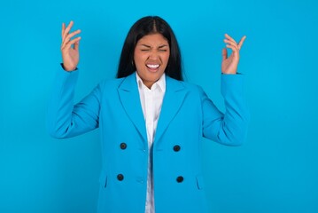 young hispanic businesswoman wearing blue blazer over blue background goes crazy as head goes...