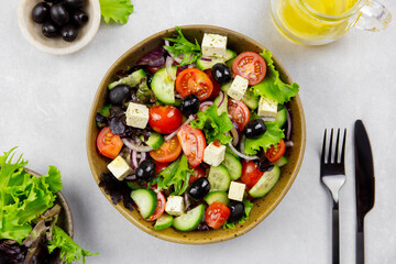 Fresh greek salad with cherry tomato, cucumber, lettuce, black olive, feta cheese and olives oil on gray concrete background. 