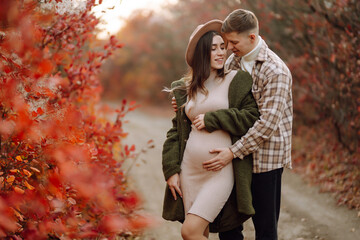 Happy and young pregnant couple in autumn park. People, lifestyle, relaxation and vacations concept.