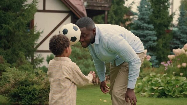 African dad and son play with a ball near the house on the lawn.Multiracial Family,Mixed Race,Diverse People,Multiethnic Relations