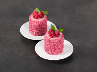 Vegan dessert. Raspberry mousse cream cakes of cylindrical shape, on a plate. Dark grey background