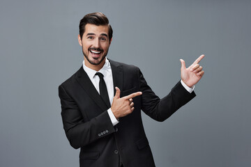 Man businessman smiles happily with teeth raised hands up showing finger in business suit with tie on dark gray background