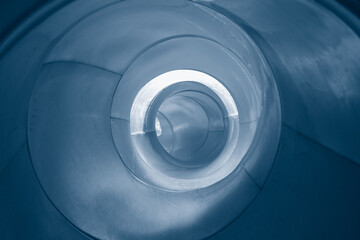 Abstract black spiral swirl inside a big shiny metal pipe, cold blue toned black and white