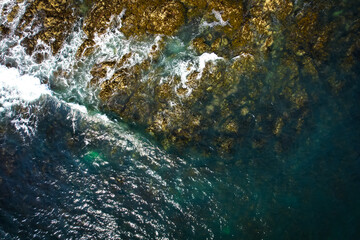 Ocean waves on rocks aerial view. St Cwyfan Church in the sea, Anglesey, Wales