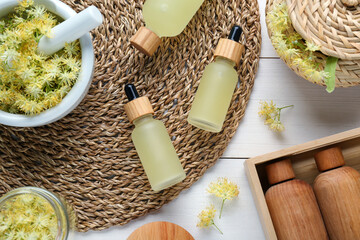Flat lay composition with bottles of essential oil and linden flowers on white wooden table