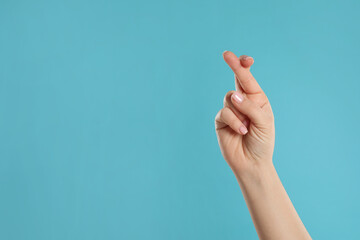 Woman holding fingers crossed on light blue background, closeup with space for text. Good luck...