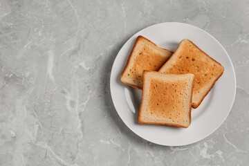 Plate with slices of delicious toasted bread on gray marble table, top view. Space for text