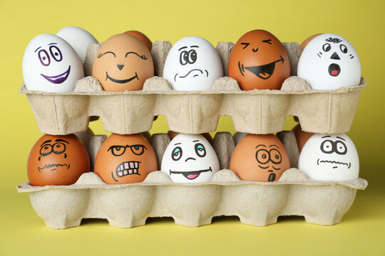 Eggs with different drawn faces in cardboard packages on pale yellow background - Powered by Adobe