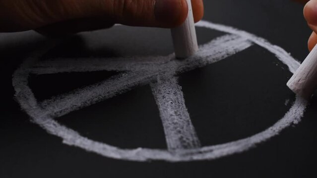 Hands drawing peace symbol with white chalks on blackboard