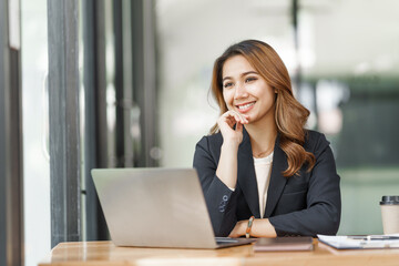 Confident pretty asian business woman working with laptop while doing some paperwork at the office workplace.