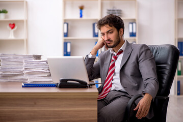 Fototapeta premium Young male employee unhappy with excessive work in the office