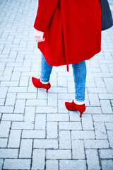 Middle-aged woman walking to a job interview dressed in blue jeans and red coat looking to the side. Cobblestone background. Copy space Business executive woman.