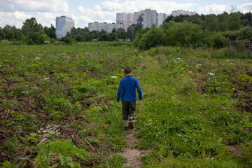 Fototapeta na wymiar Child walks by nature. Schoolboy walks alone in summer. Boy in blue jacket on street.