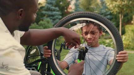 African dad helps his son repair his bike on the lawn near the house.Multiracial Family,Mixed Race,Diverse People,Multiethnic Relations