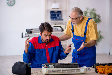 Two male repairmen repairing air-conditioner