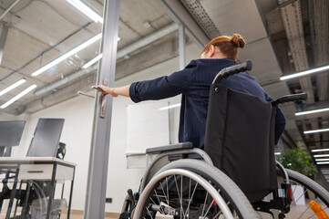Fototapeta na wymiar Red-haired caucasian woman in a wheelchair trying to open the door in the office. 