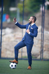 businessman taking a selfie with his cell phone with a ball inside a soccer field © Imaxepress