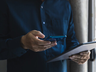 Young businessman working with modern devices, digital tablet computers and mobile phones. A man standing in the house with his phone and tablet in the morning.