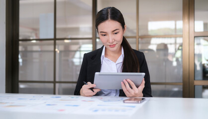 Attractive young businesswoman sitting in modern office and using digital tablet..