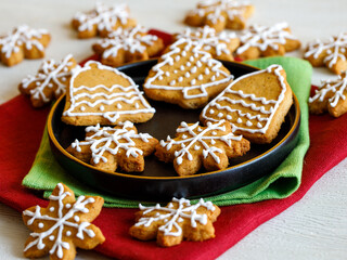 Fototapeta premium Homemade gingerbread cookie in shape of snowflakes and bells decorated with icing on black plate on green and red napkins. Traditional Christmas food. Christmas and New Year holiday concept.