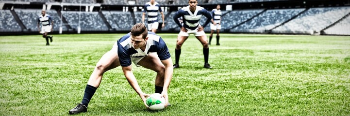 Digital composite image of rugby player picking up the ball in sports stadium