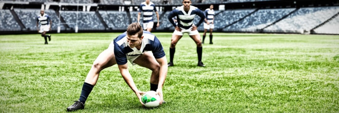 Digital composite image of rugby player picking up the ball in sports stadium