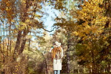 Fototapeta premium A young red-haired woman walks through the autumn park. A girl in a beige hat looks at the autumn forest
