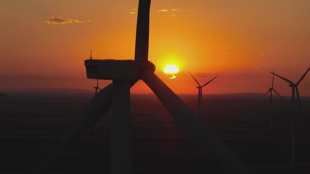 Aerial drone view of a flying over the windmill field. Landscape view of wind turbines spinning with orage sun in the background
