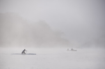 Kayaker with fishing boat in morning mist 