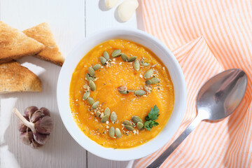 pumpkin puree hot soup, spicy autumn vegan meal with pumpkin seeds, croutons and garlic. top view.